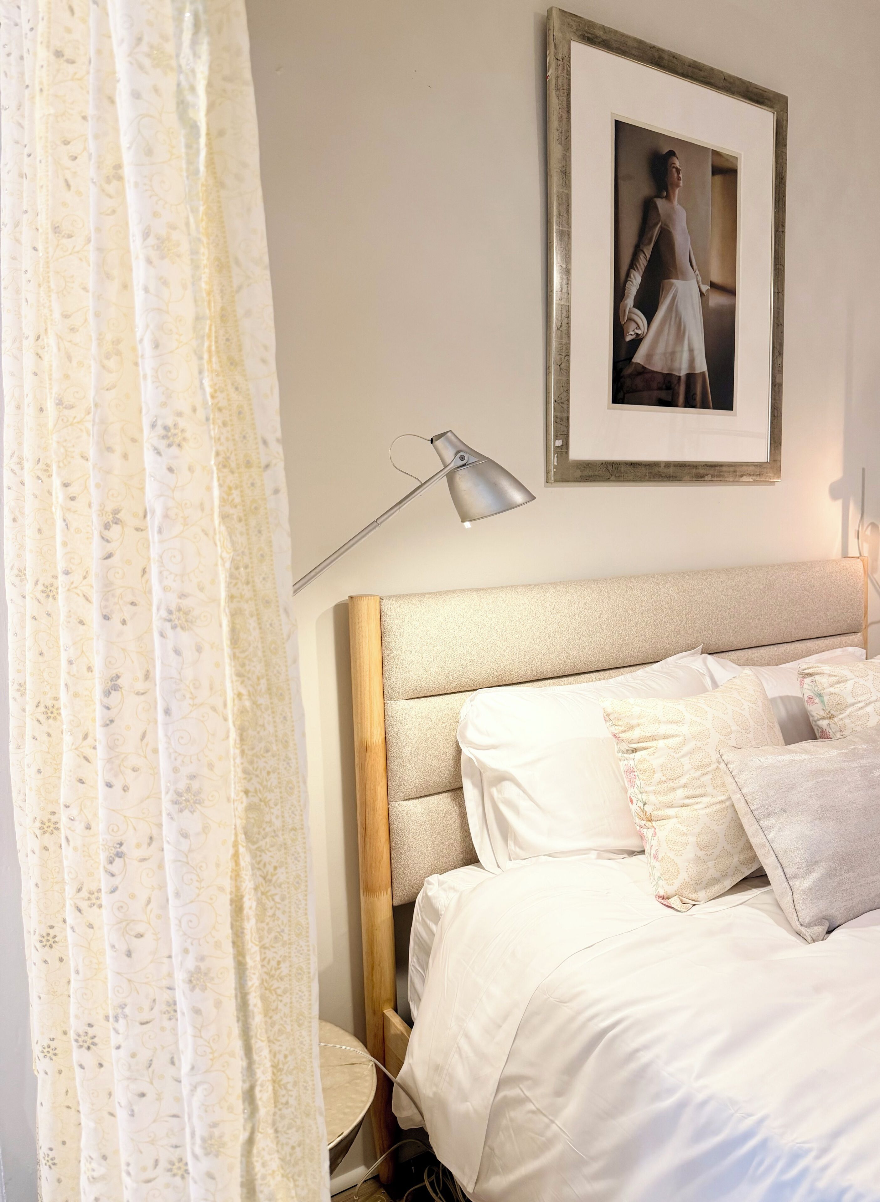 A bedroom with a bed, a lamp, a framed picture on the wall, and a curtain.