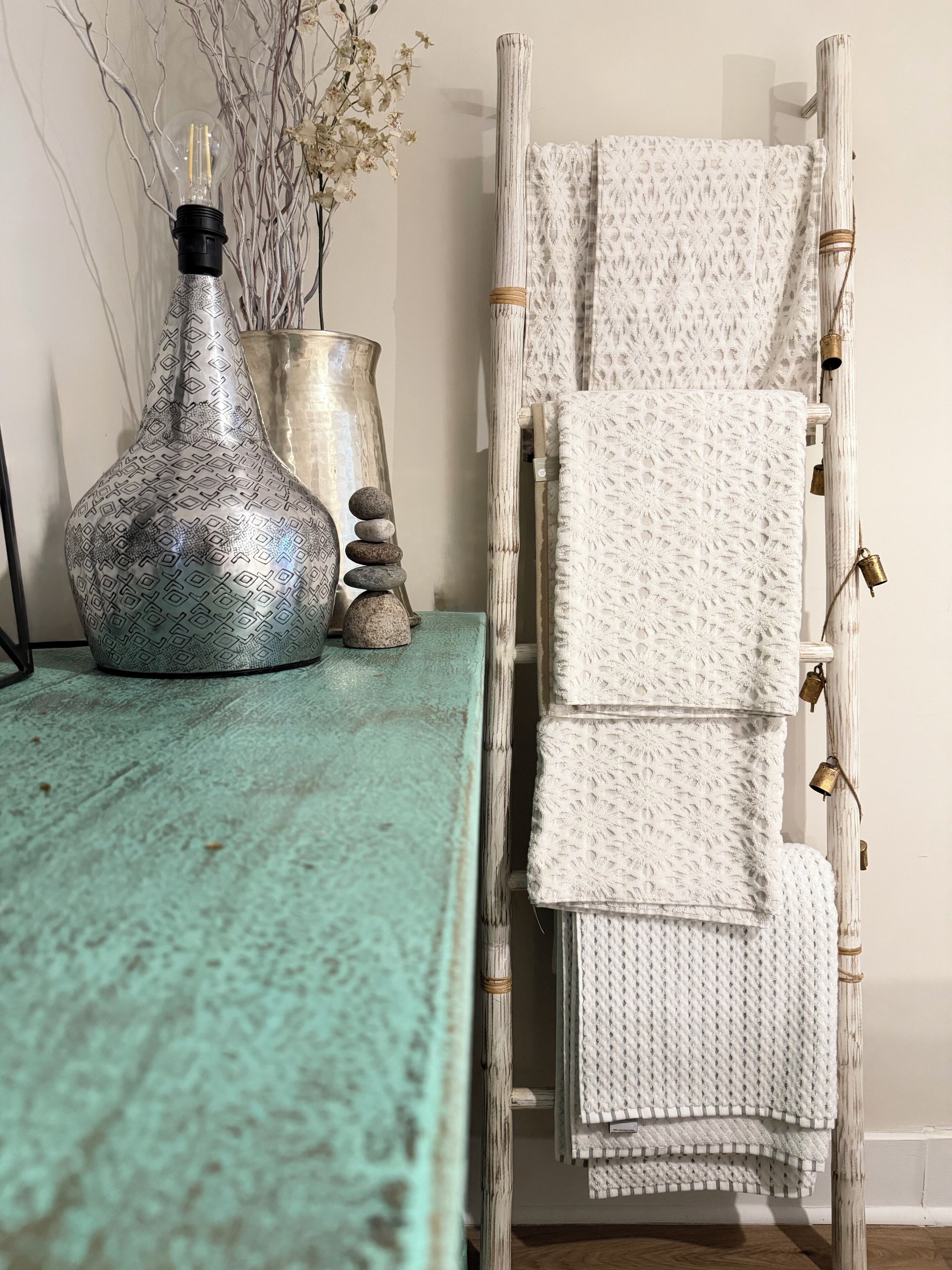 A rustic interior with a textured teal table, a decorative vase, a stack of stones, and a white woven chair.