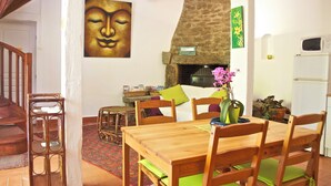 Un coin repas avec une table et des chaises en bois, une cheminée en pierre et un tableau représentant un Bouddha accroché au mur.