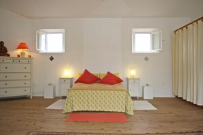 Ein Schlafzimmer mit einem Bett, zwei Nachttischen, einer Kommode, zwei Fenstern und einem Vorhang.