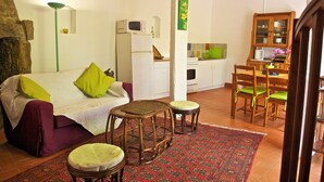 Un espace de vie compact comprenant un canapé, deux tabourets, une table à manger avec des chaises, un coin cuisine et un meuble de rangement.