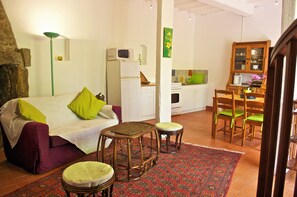 Ein kompakter Wohnbereich mit einer Couch, zwei Hocker, einem Esstisch mit Stühlen, einer Küchenzeile und einem Schrank.