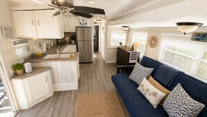Una cocina compacta con una isla central, un área de comedor con un sofá azul y un ventilador de techo.