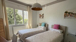 Une chambre d’hôtel avec deux lits, un bureau, une chaise, une fenêtre avec des rideaux et un tableau au mur.
