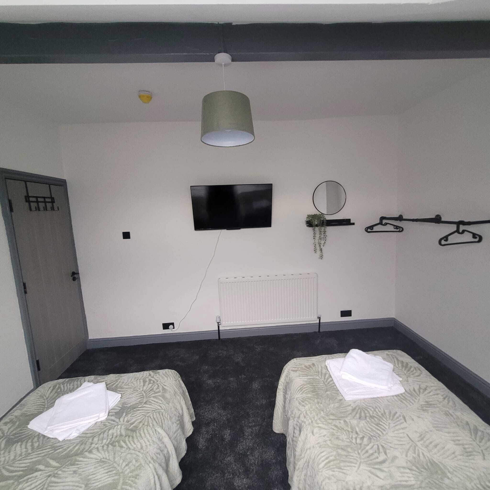 Ein Zimmer mit zwei Betten, einem Fernseher, einem Heizkörper, einer Tür und einer Pendelleuchte.