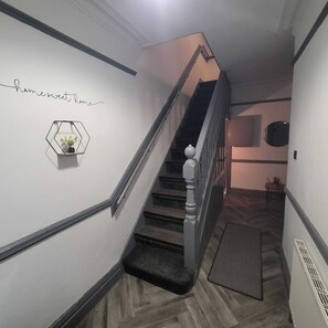 Un escalier avec une rampe, un panneau fixé au mur et une étagère hexagonale sur laquelle est posée une plante.