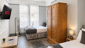 Ein Hotelzimmer mit zwei Betten, einem Holzschrank, einem Fernseher und einem Schreibtisch mit einer Pflanze.