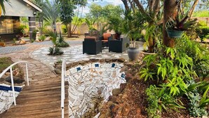 Een terras met een mozaïekzwembad, tuinmeubilair en weelderige beplanting.