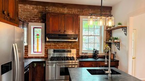 A kitchen with wooden cabinets, a stainless steel refrigerator, a gas stove, and a window with a view of greenery.