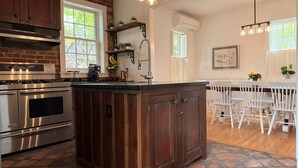 A kitchen with a central island, stainless steel appliances, and a dining area with white chairs.