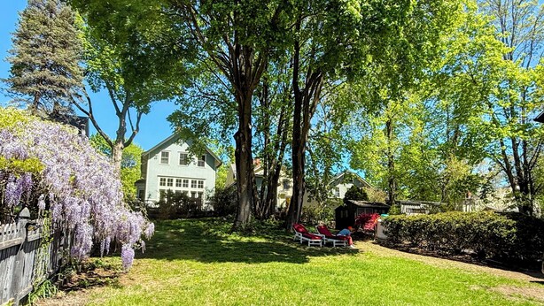 A residential backyard with a lawn, a white house, and a wooden fence.