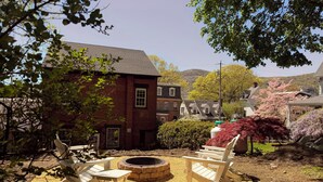 A patio with Adirondack chairs, a fire pit, and a brick building in the background.