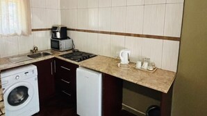 A compact kitchen with a washing machine, a small fridge, a microwave, and a sink. - Studio in Golden Acres – Kwekwe - 2371 (Kwekwe)