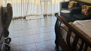 A bedroom with a bed, a chair, a small table, curtains, and a wall with a poster. - Studio in Golden Acres – Kwekwe - 2371 (Kwekwe)