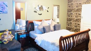 A bedroom with a bed, bedside tables, a nightstand, a lamp, a mirror, and a stone wall. - Studio in Golden Acres – Kwekwe - 2371 (Kwekwe)