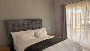 Een slaapkamer met een groot bed, een hoofdbord, twee nachtkastjes en een raam met gordijnen.