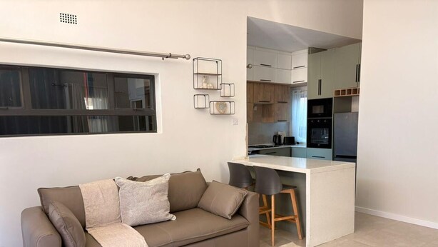 Een moderne woonkamer met een bank, een salontafel en een zichtbare keuken door een open doorgang.