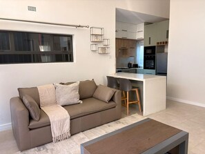 Un salon moderne avec un canapé, une table basse et un coin cuisine visible à travers une porte ouverte.