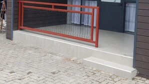 Een modern gebouw met een overdekt terras, een rode balustrade en een trap naar de tweede verdieping.
