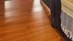 Una habitación con piso de madera, un sofá oscuro, un plaid estampado y un espejo en la pared.