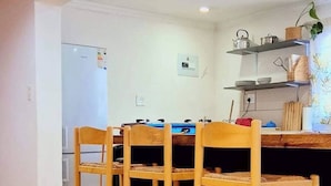 Un comedor con sillas y una mesa de madera, una cocina con estanterías y un refrigerador, y un techo de madera.