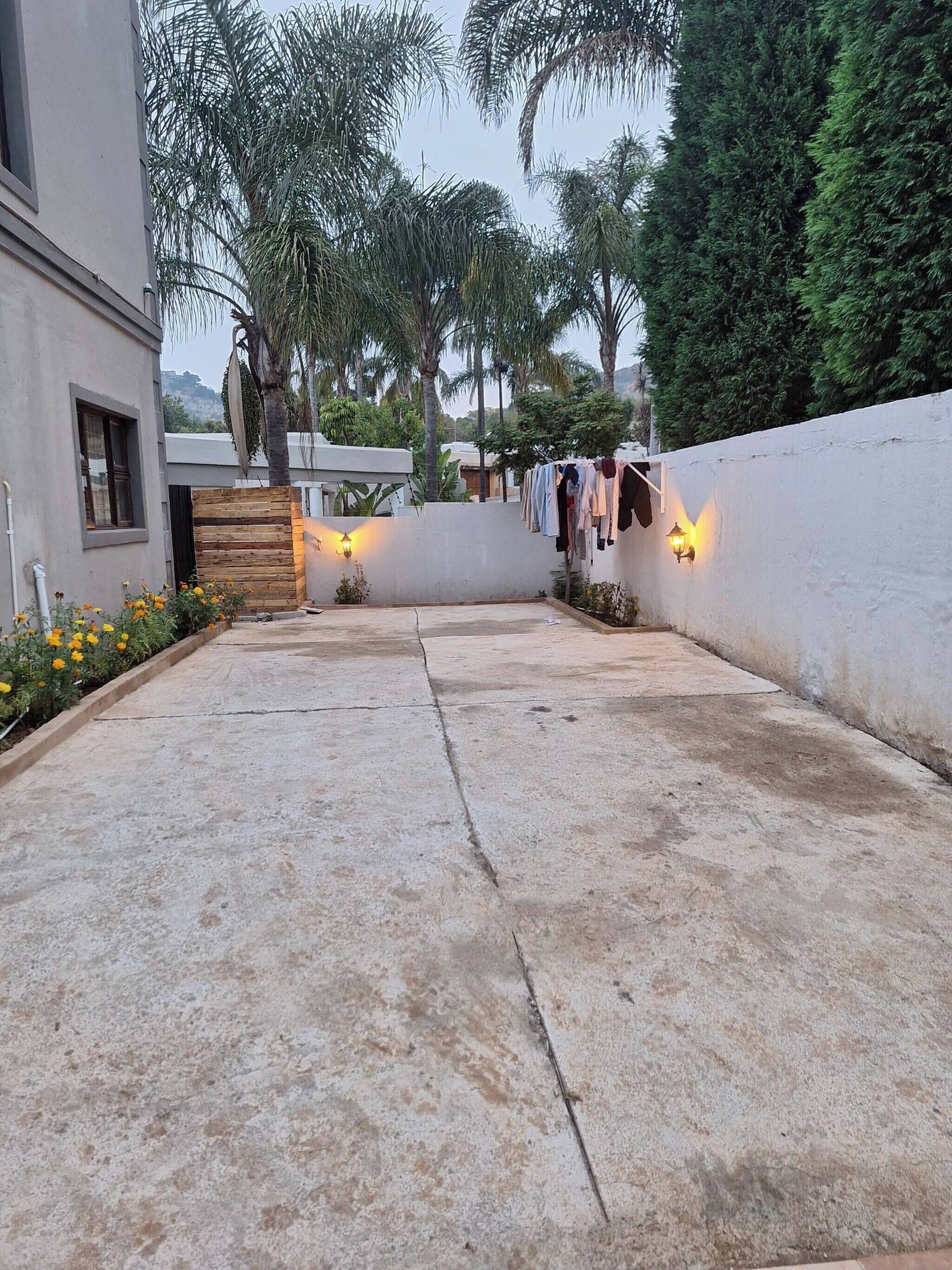 A courtyard with a concrete floor, a wooden fence, a clothesline, and a wall-mounted light fixture.