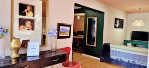 Quarto com escrivaninha, cadeiras, televisão, quadros e espelho.