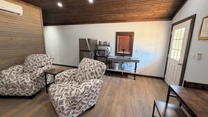 A modern living room with patterned sofas, a kitchen area with appliances, and a wooden ceiling. - BRAND NEW!!  1-bedroom cabin with 2  Queen beds. Near PICKWICK LAKE (Iuka)