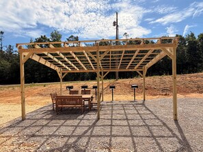 Puinen pergola, jonka alla on kivimurskapohja ja penkkejä.