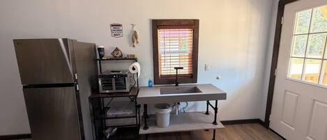 A compact kitchen with a refrigerator, a sink, a window with blinds, and a wooden ceiling.