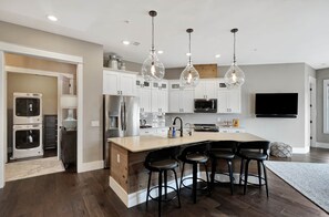 A modern kitchen with white cabinets, stainless steel appliances, a large island with bar stools, and pendant lighting.