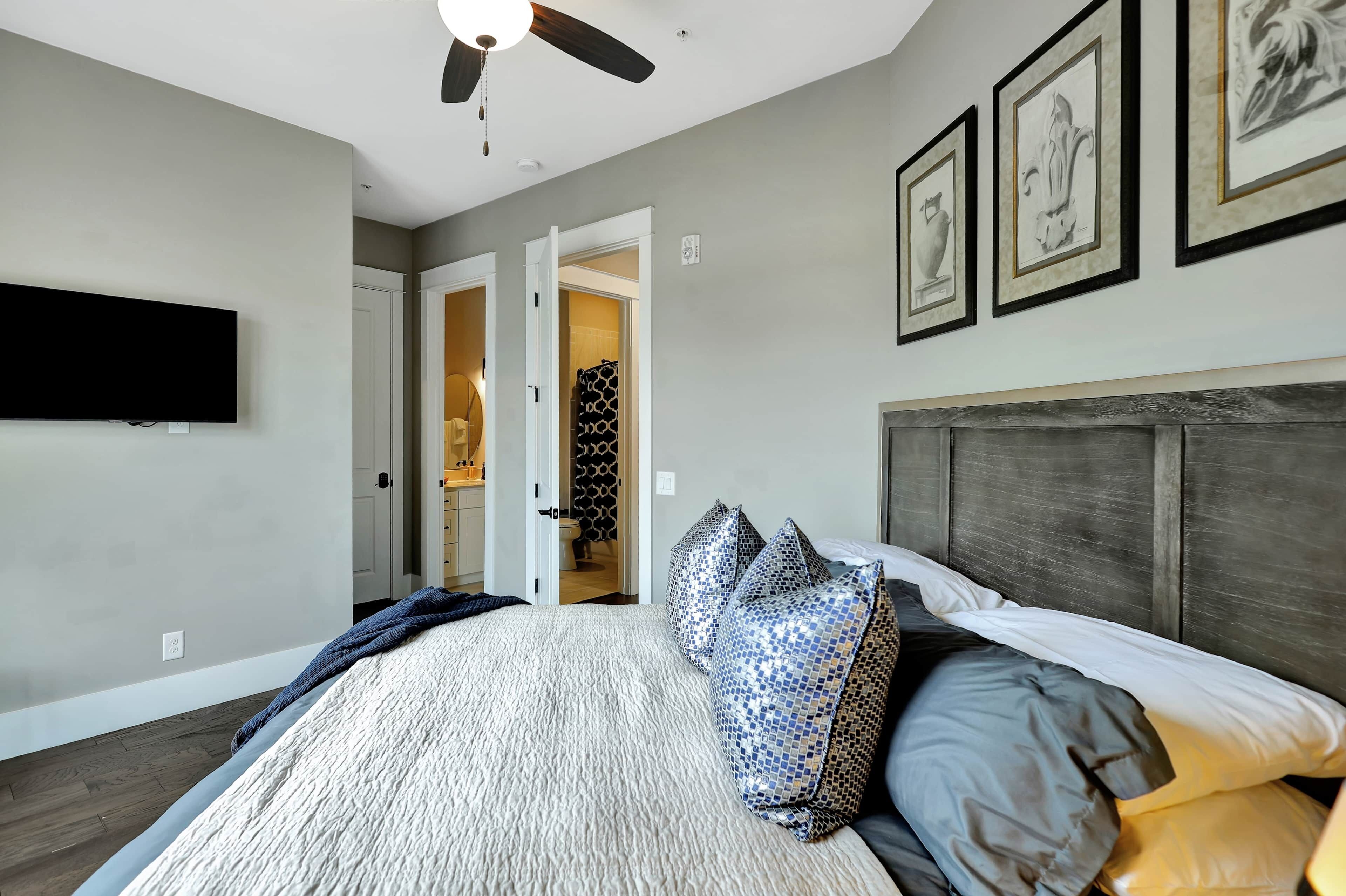 A bedroom with a bed, a ceiling fan, a TV, and framed artwork on the wall.