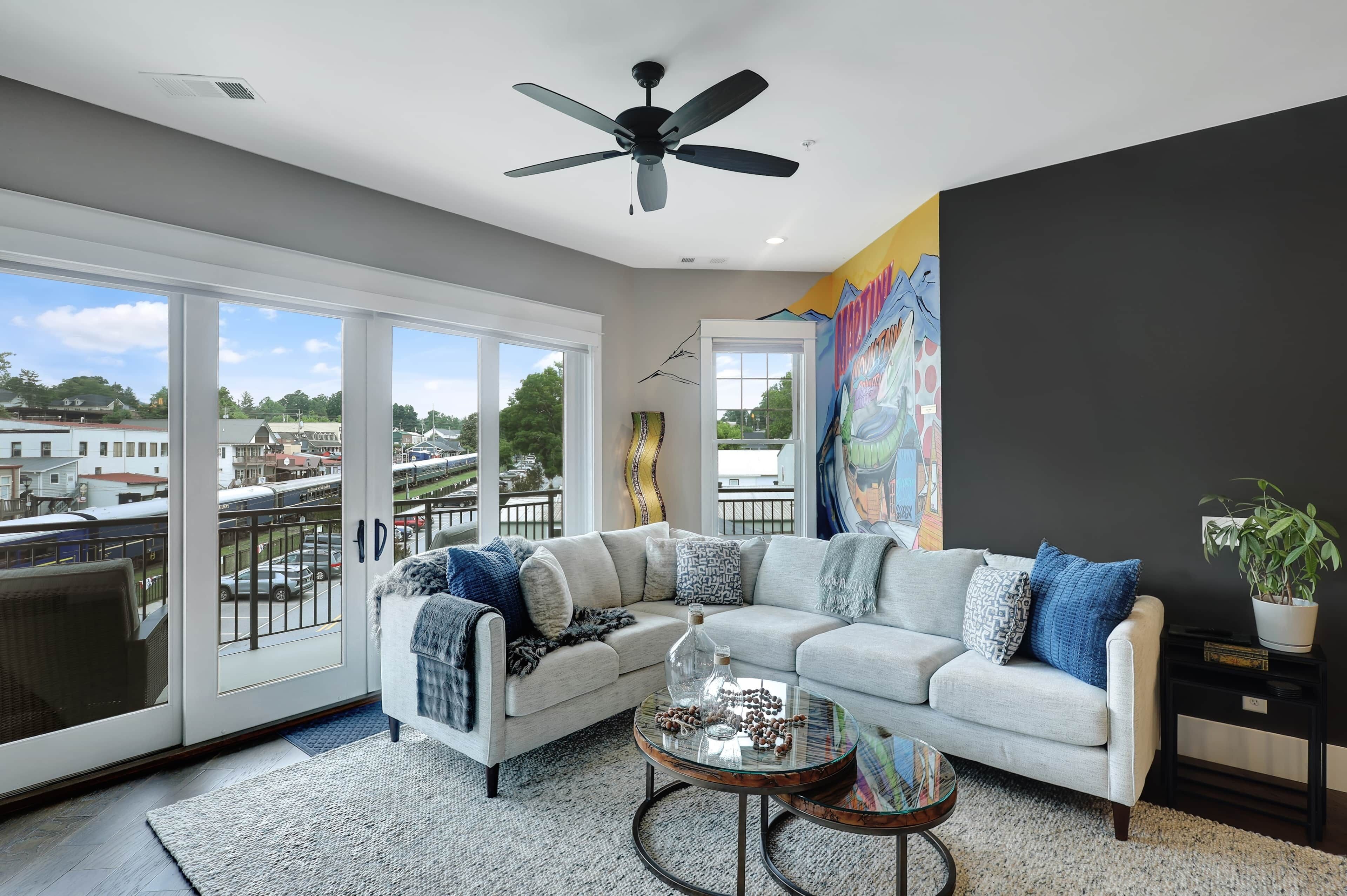 A modern living room with a sectional sofa, a glass coffee table, and a balcony with a view of the city.