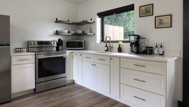 A modern kitchen with white cabinetry, stainless steel appliances, and a window with a view of greenery. - Steps from the Lake- Sauna + Hot Tub. Entire 7 Unit Inn (Jones)