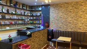 Angolo bar con bancone, scaffali pieni di bottiglie, un altoparlante e una zona con tavolo e sedie.