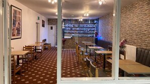 Un ristorante con tappeto a motivi, tavoli e sedie in legno, un'area bar con scaffali pieni di bottiglie e una parete in pietra.