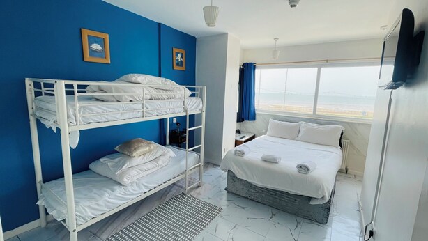 Una camera d'albergo con letti a castello, un letto singolo, un'ampia finestra con vista e una TV a schermo piatto.