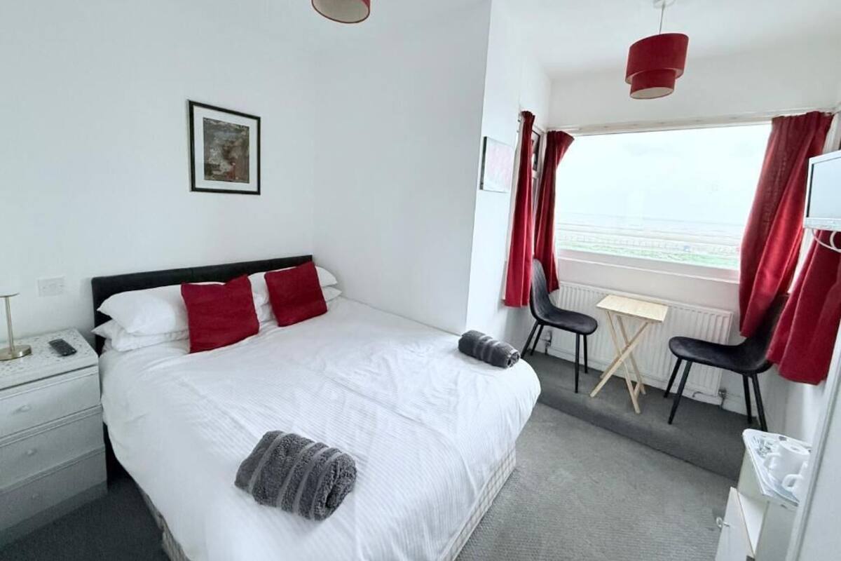 A hotel room with a bed, a desk, two chairs, a window with curtains, and a small table.