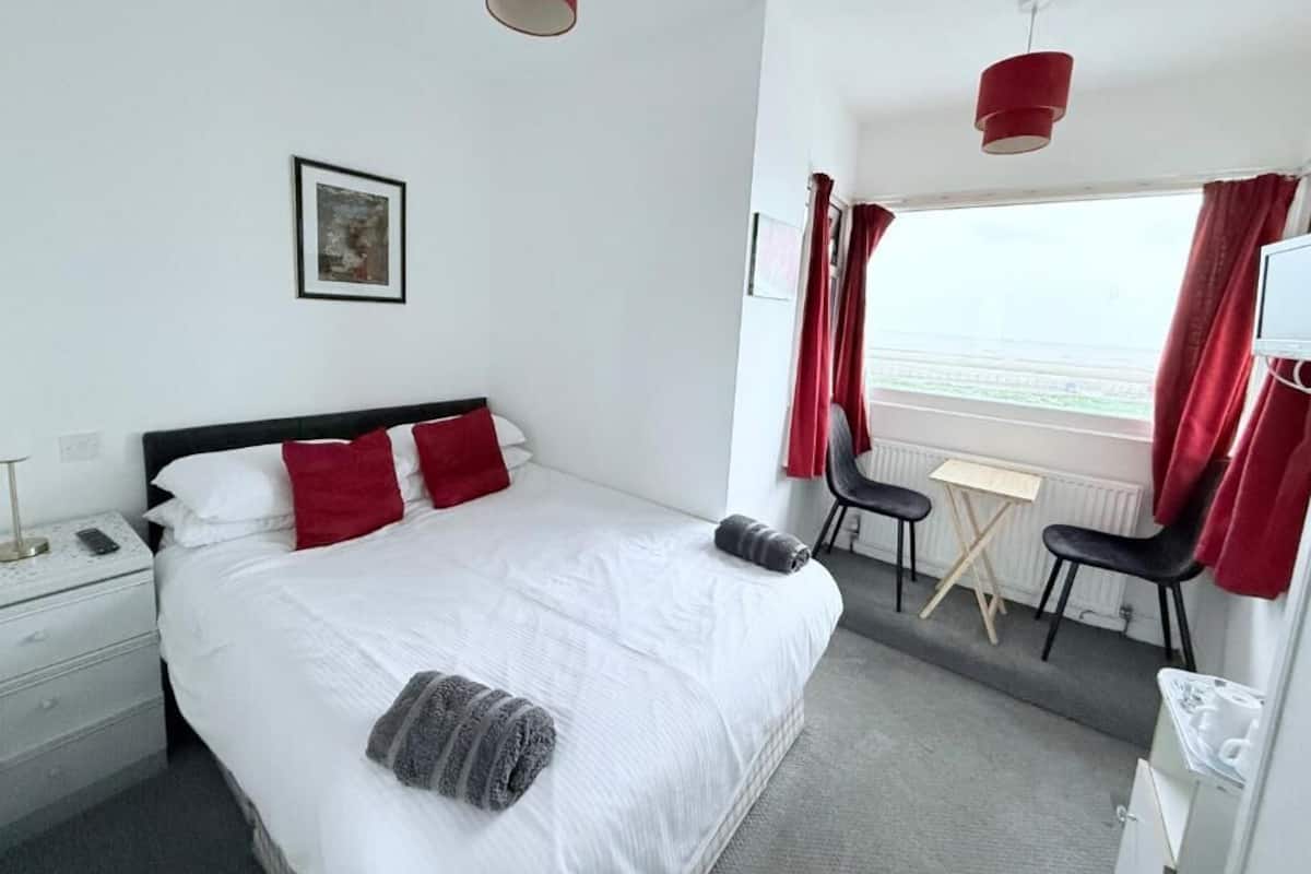 Hotellihuone, jossa on sänky, työpöytä, kaksi tuolia, ikkuna verhoilla ja pieni pöytä.