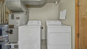 Een wasserette met twee witte wasmachines en drogers, een boiler en een geventileerd afvoersysteem.