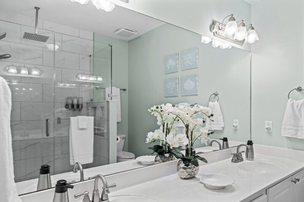 Een moderne badkamer met een grote spiegel, twee wasbakken, een douche en decoratieve orchideeën.