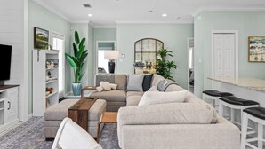 A living room with a sectional sofa, a television, a ceiling fan, and a dining area with bar stools. - Private 30A Beach Retreat - Coastal Backyard Oasis (Santa Rosa Beach)
