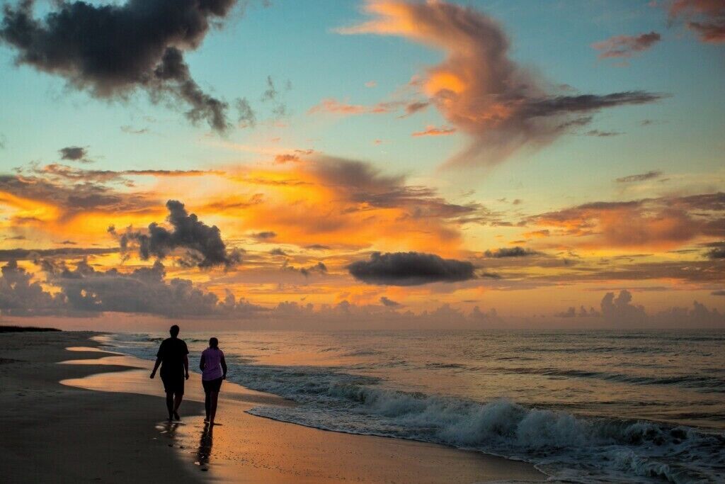 Twee mensen wandelen langs het strand bij zonsondergang.