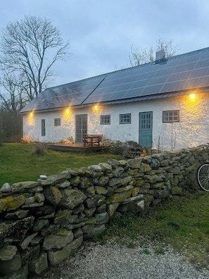 A stone house with a solar panel roof, a green door, and a stone wall in the foreground.