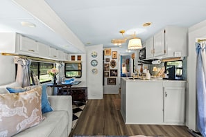 A compact RV interior with a kitchenette, dining area, and a living space with a sofa and decorative pillows. - French Country Farm Stay RV–Sunsets, Horses & Cozy Cottage Charm in Fairhope, AL (Fairhope)