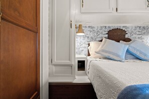 A bedroom with a wooden wardrobe, a white bedside table with a lamp, a bed with patterned bedding, and a decorative headboard. - French Country Farm Stay RV–Sunsets, Horses & Cozy Cottage Charm in Fairhope, AL (Fairhope)