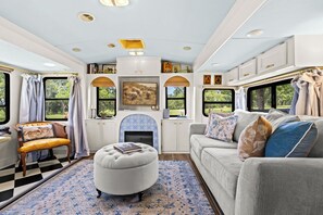A cozy RV interior with a sofa, ottoman, and a fireplace. - French Country Farm Stay RV–Sunsets, Horses & Cozy Cottage Charm in Fairhope, AL (Fairhope)