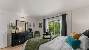 Un dormitorio con cama, cómoda, espejo y ventana con vistas al verdor.