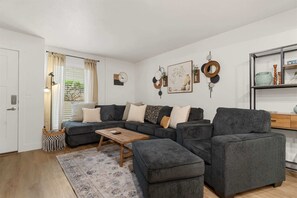 A living room with a sectional sofa, a coffee table, and a rug. There is a door to the left and a shelf with decorative items on the right. - Roark Creek View  Pool & Gym (Branson)