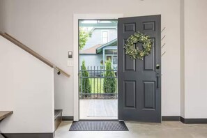 Eine dunkelgraue Tür mit einem Kranz, einem Holzgeländer und einem Metallgitter, das zu einem Haus führt.
